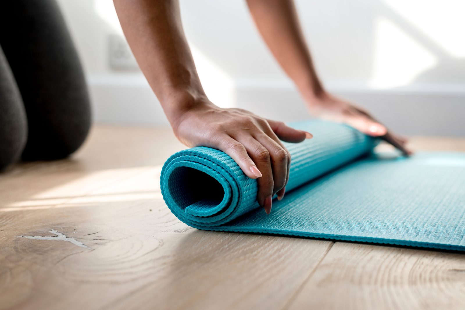 A person rolling up a blue yoga mat.